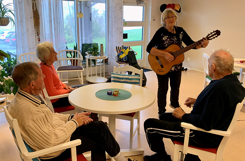 Sylvia Sandin sjunger för tre äldre personer som sitter vid ett runt bord.