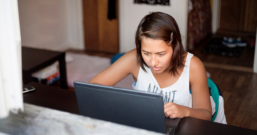 Ung flicka med mörkt hår sitter vid datorn.
