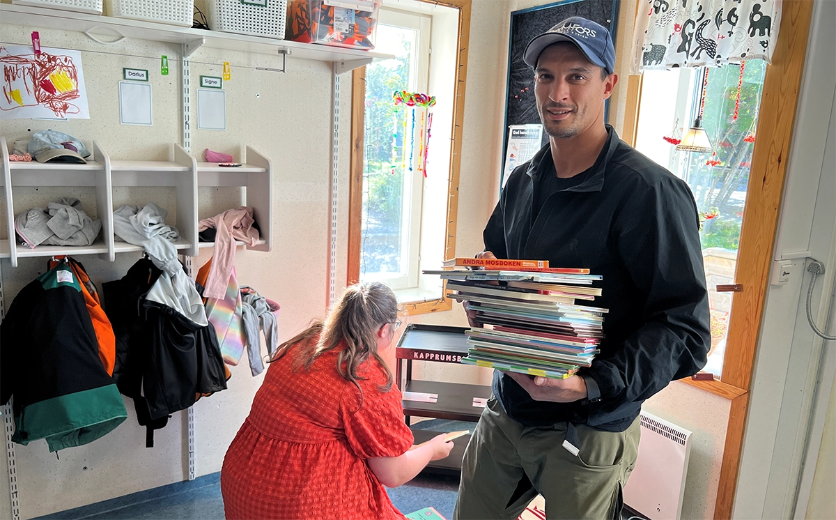 Yemel Aisa håller i en trave böcker. Elin Gustavsson rengör bokhyllan.