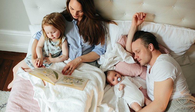 Familj i sängen som läser en bok.