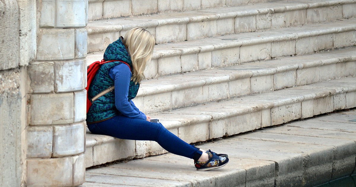 En ung tjej sitter på en stentrappa och hänger med huvudet.