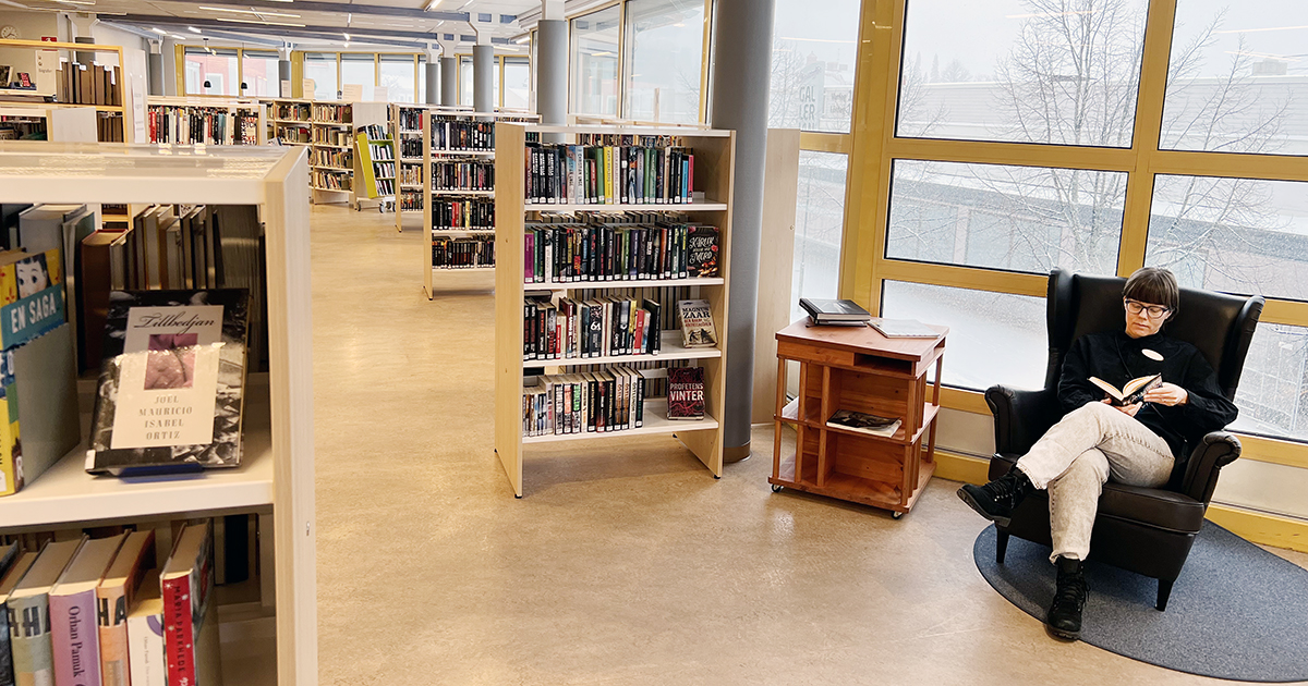 Bibliotekarie Victoria Jonsson sitter i en fåtölj och läser en bok. Man ser också en massa bokhyllor fyllda av böcker.