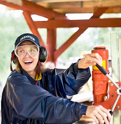 Kvinna med skyddsglasögon och hörselkåpor bredvid en industrimaskin
