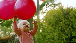 Liten flicka med röda ballonger.